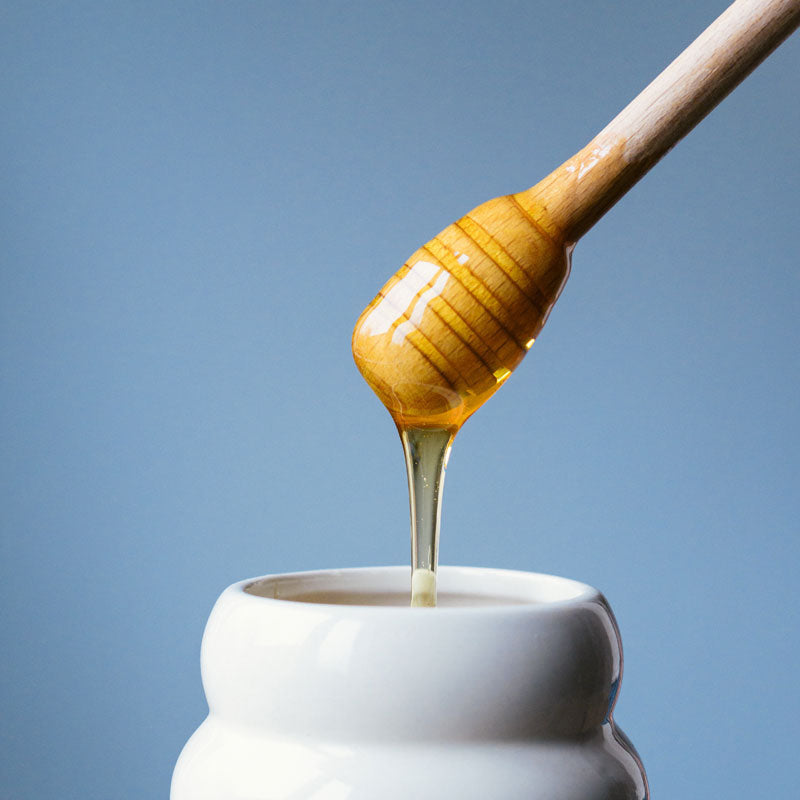 A honey dipper dripping honey into a honeypot
