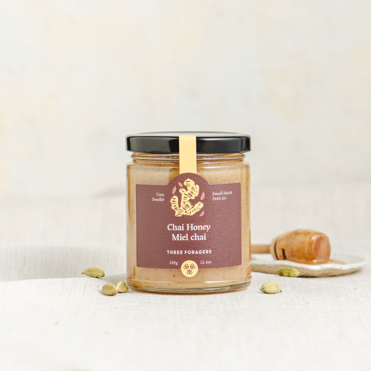 A jar of Three Foragers Chai Honey with a honey dipper next to it